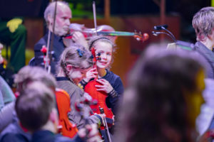 Young girl holding a violin and smiling.